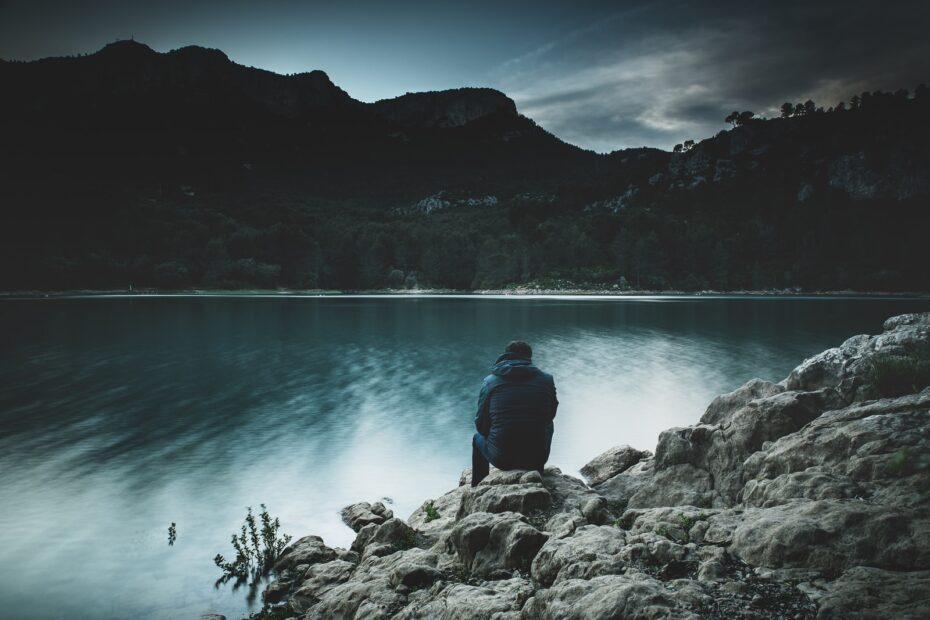 a man sits on a rock staring across a lake at dusk