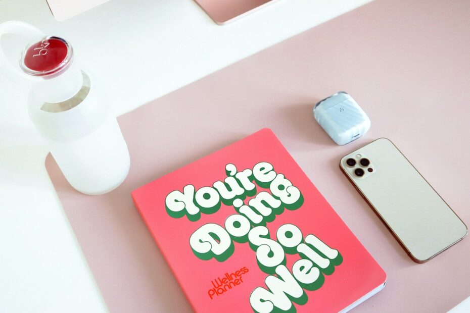 a pink book sitting on top of a desk next to a cell phone