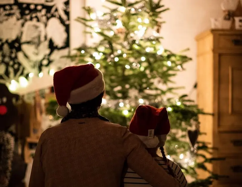 selective focus photography of a child and adult snuggling in front of a christmas tree